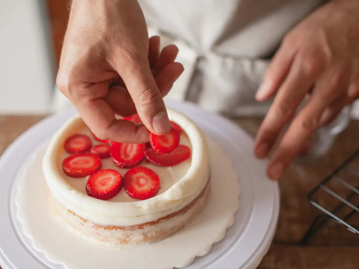 Mãos de confeiteiro dispondo fatias de morango sobre um bolo