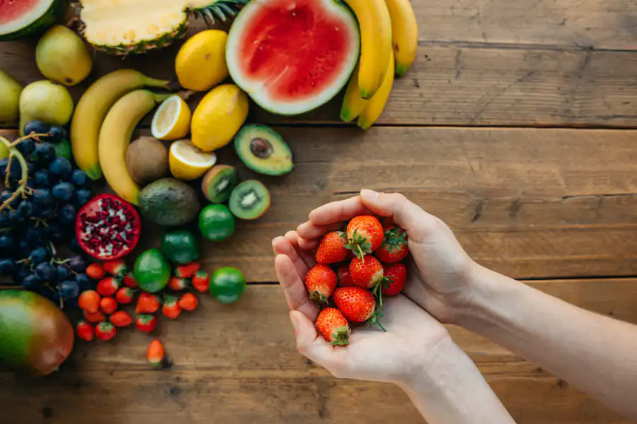 Mãos segurando morangos sobre mesa com frutas variadas