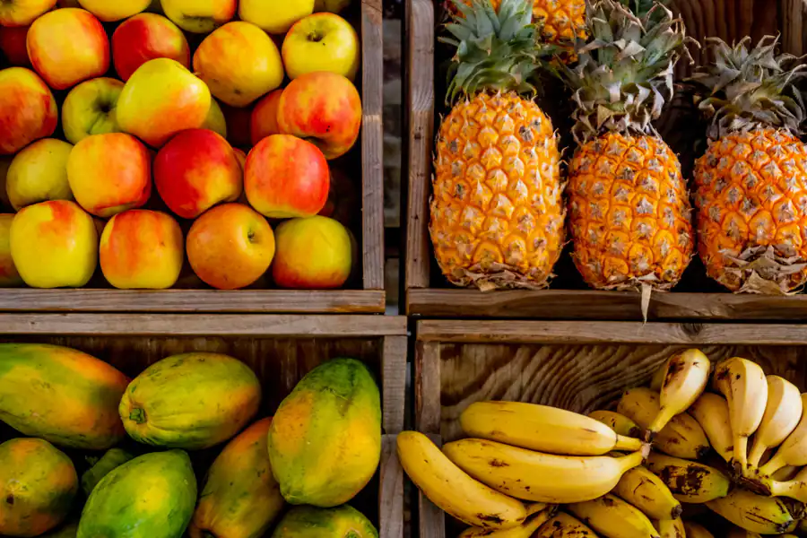 Maçã, abacaxi, mamão e banana em engradados de madeira