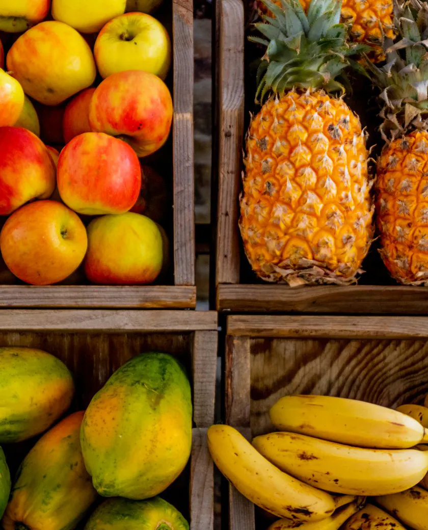 Maçã, abacaxi, mamão e banana em engradados de madeira